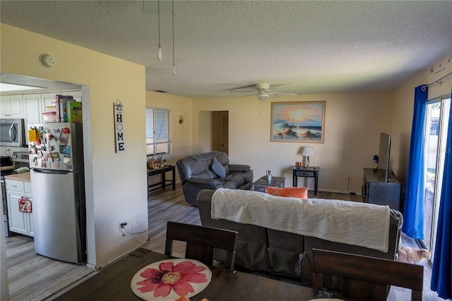 living room featuring light hardwood / wood-style flooring, a textured ceiling, and ceiling fan