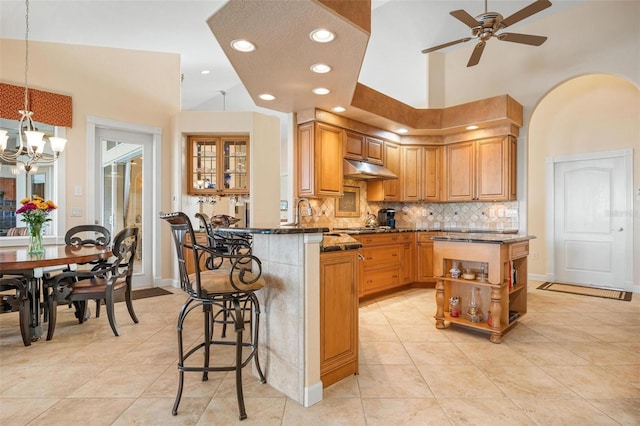 kitchen featuring a kitchen breakfast bar, kitchen peninsula, dark stone counters, decorative light fixtures, and ceiling fan with notable chandelier