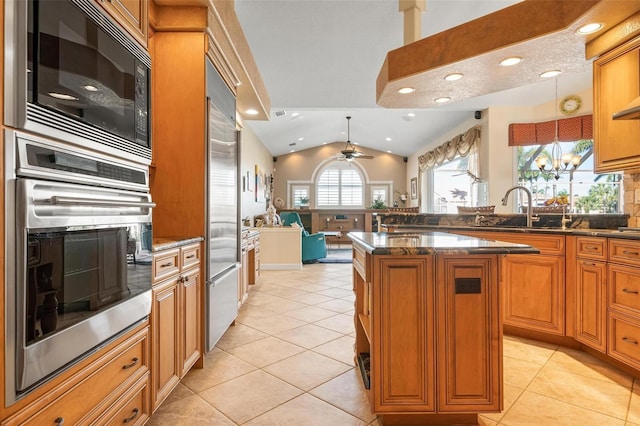 kitchen featuring built in appliances, sink, a center island, light tile patterned flooring, and decorative light fixtures