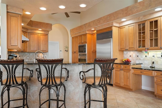 kitchen with built in appliances, dark stone countertops, a textured ceiling, and a breakfast bar