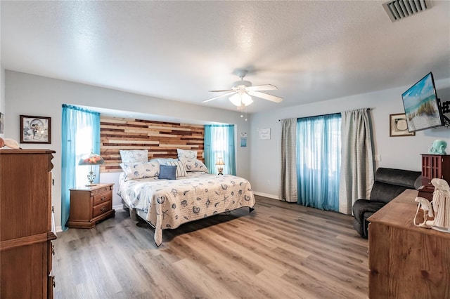 bedroom featuring wooden walls, wood-type flooring, a textured ceiling, and ceiling fan