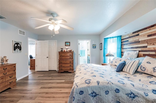 bedroom with wood walls, ensuite bathroom, dark wood-type flooring, and ceiling fan