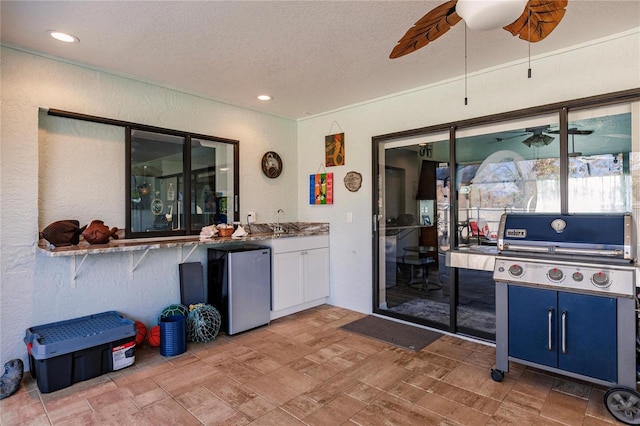 kitchen featuring ceiling fan, a textured ceiling, stainless steel refrigerator, blue cabinetry, and sink