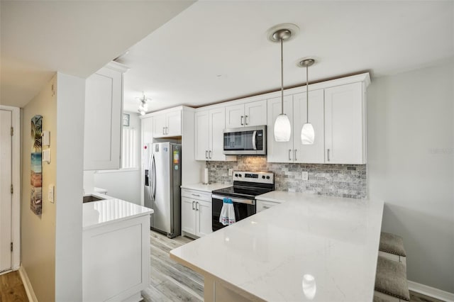 kitchen with kitchen peninsula, hanging light fixtures, stainless steel appliances, white cabinets, and light hardwood / wood-style flooring