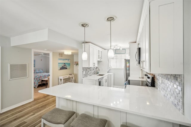 kitchen featuring appliances with stainless steel finishes, kitchen peninsula, white cabinetry, decorative light fixtures, and light hardwood / wood-style flooring