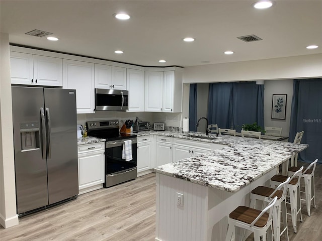 kitchen with appliances with stainless steel finishes, sink, kitchen peninsula, light hardwood / wood-style floors, and white cabinets