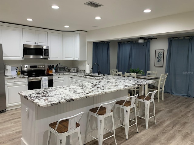 kitchen with a breakfast bar, white cabinetry, stainless steel appliances, and sink