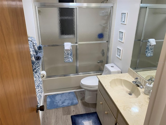 full bathroom with toilet, bath / shower combo with glass door, hardwood / wood-style flooring, and vanity