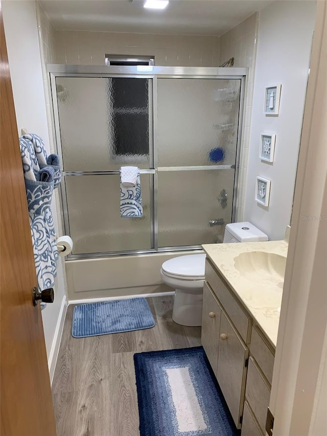 full bathroom with vanity, combined bath / shower with glass door, hardwood / wood-style floors, and toilet