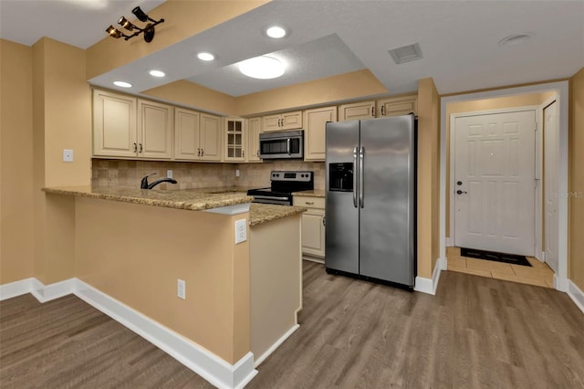 kitchen featuring decorative backsplash, kitchen peninsula, stainless steel appliances, and light wood-type flooring