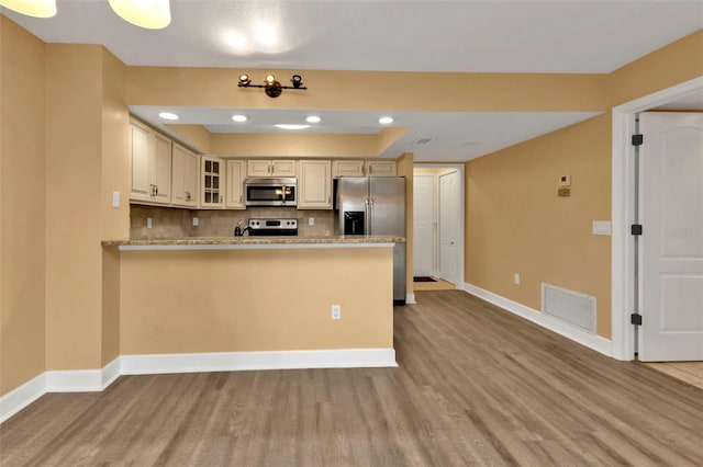 kitchen with appliances with stainless steel finishes, light hardwood / wood-style flooring, tasteful backsplash, and light stone counters