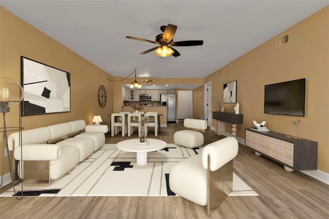 living room with ceiling fan with notable chandelier and light wood-type flooring