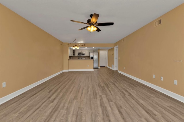 unfurnished living room featuring ceiling fan with notable chandelier and light hardwood / wood-style floors