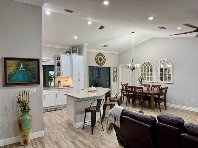 kitchen with lofted ceiling, ornamental molding, light stone countertops, pendant lighting, and white cabinets