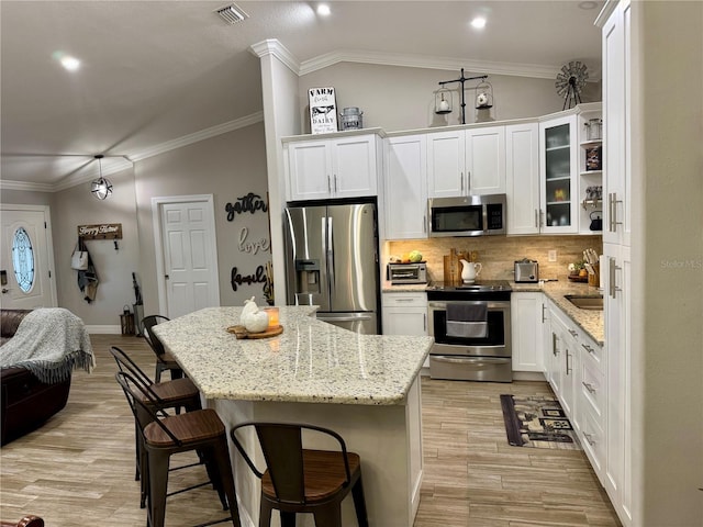 kitchen with appliances with stainless steel finishes, a breakfast bar, white cabinetry, and light stone countertops