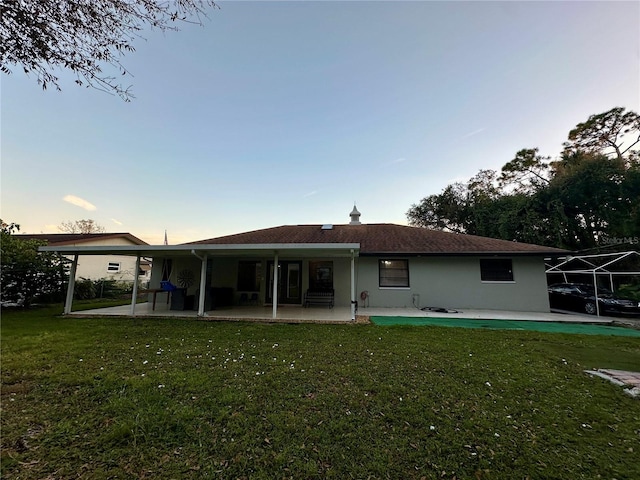 back house at dusk featuring a patio area and a lawn