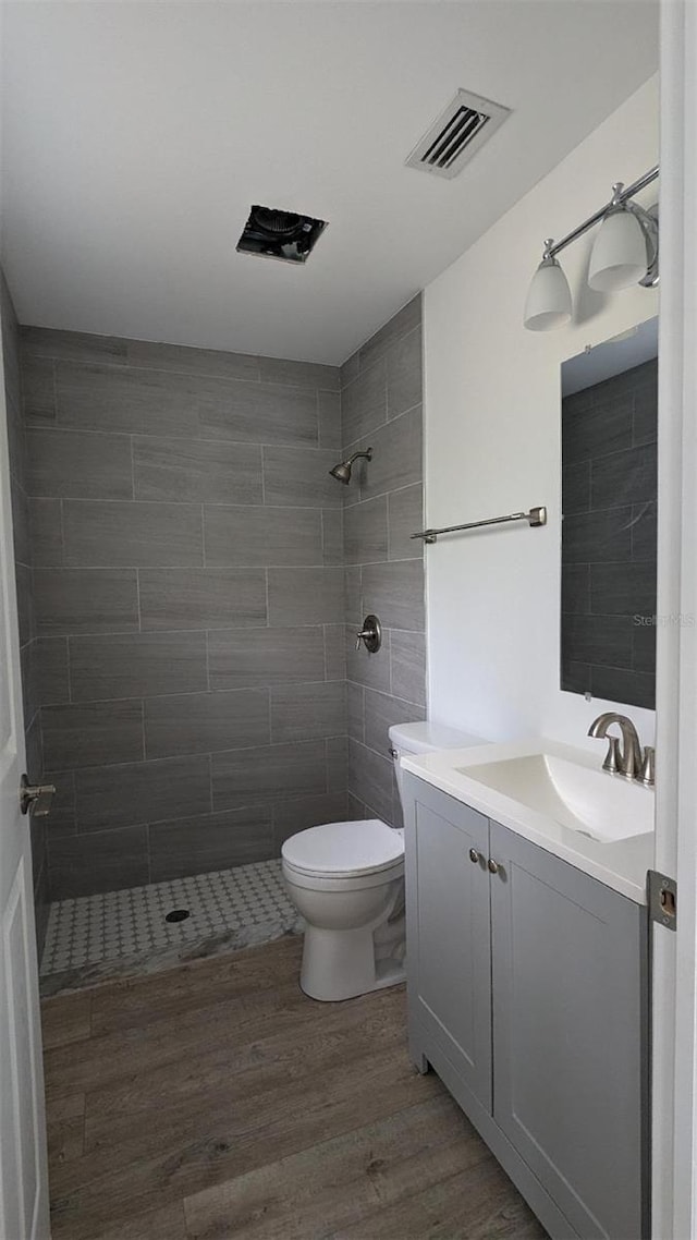 bathroom with wood-type flooring, vanity, a tile shower, and toilet