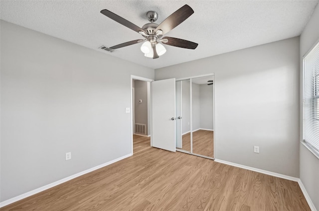 unfurnished bedroom with a textured ceiling, light wood-type flooring, a closet, and ceiling fan