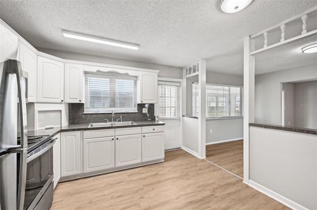 kitchen with light wood-type flooring, tasteful backsplash, sink, stainless steel range oven, and white cabinets