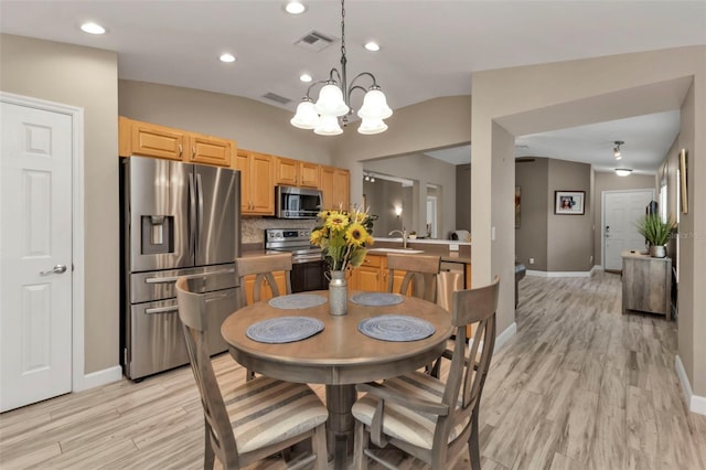 dining room featuring light hardwood / wood-style floors, a chandelier, sink, and vaulted ceiling