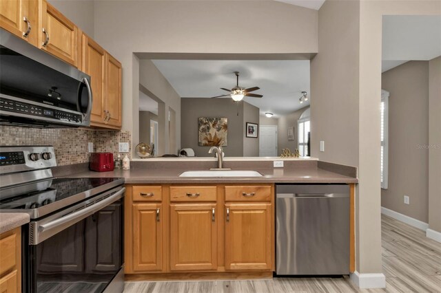 kitchen with tasteful backsplash, appliances with stainless steel finishes, sink, light wood-type flooring, and ceiling fan