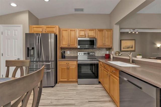 kitchen with appliances with stainless steel finishes, lofted ceiling, sink, and backsplash