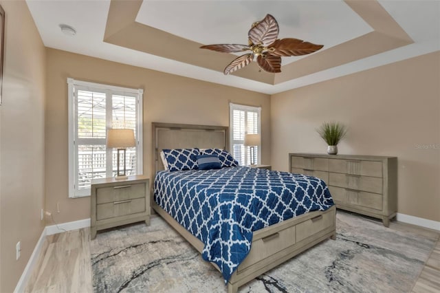 bedroom with light hardwood / wood-style flooring, ceiling fan, and a tray ceiling