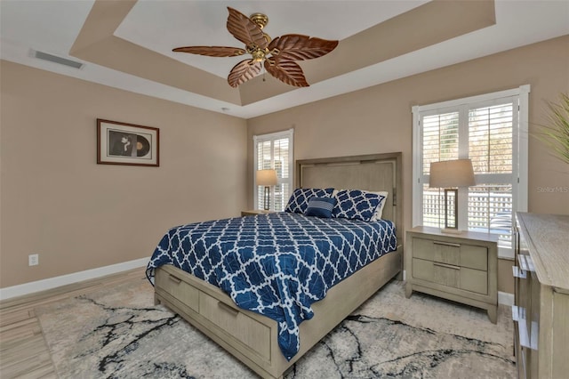 bedroom featuring multiple windows, a tray ceiling, and ceiling fan