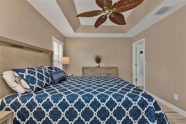 bedroom featuring a tray ceiling, wood-type flooring, and ceiling fan