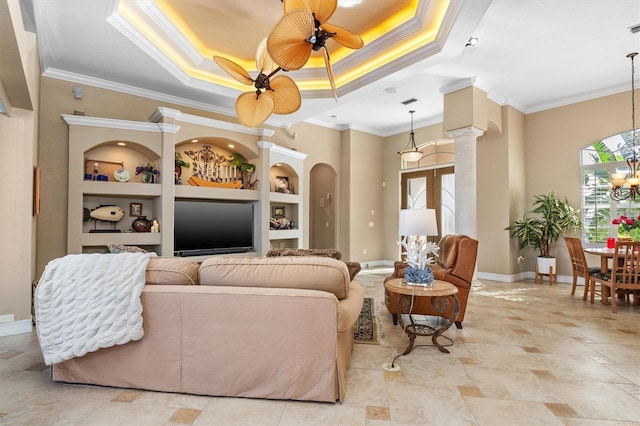 living room with ceiling fan with notable chandelier, decorative columns, a tray ceiling, crown molding, and built in shelves