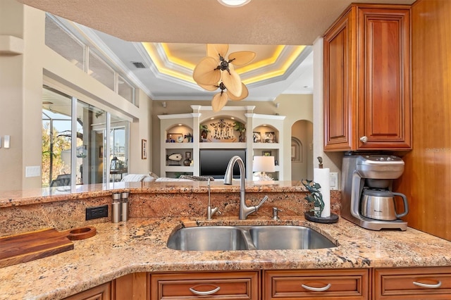 kitchen featuring light stone countertops, a raised ceiling, ornamental molding, and sink