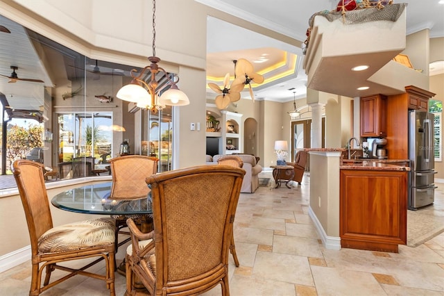 dining room with crown molding, sink, ceiling fan with notable chandelier, and decorative columns