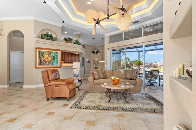 living room with ceiling fan, a raised ceiling, ornamental molding, and a high ceiling