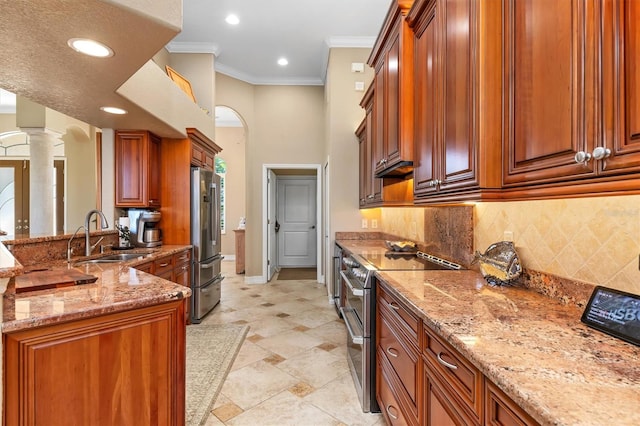 kitchen featuring light stone countertops, appliances with stainless steel finishes, sink, ornate columns, and ornamental molding