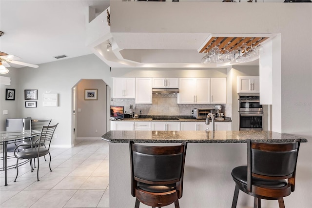 2868 Coral Way, Punta Gorda, FL 33950 - kitchen with double oven, black stovetop, backsplash, ceiling fan, and a kitchen bar