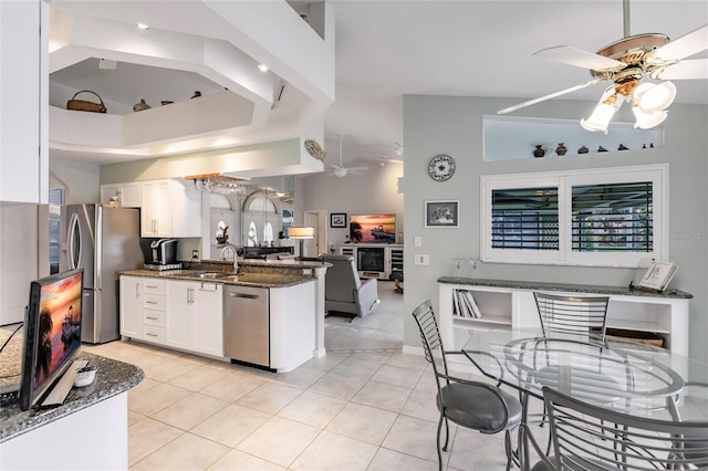 kitchen with dark stone counters, appliances with stainless steel finishes, light tile patterned floors, white cabinets, and kitchen peninsula