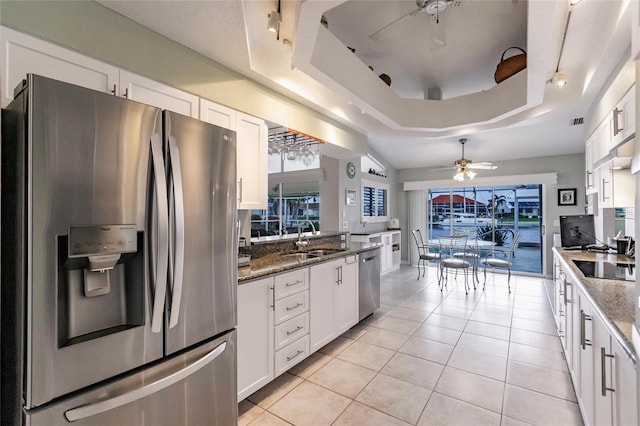 kitchen with stainless steel appliances, dark stone counters, white cabinets, sink, and a tray ceiling