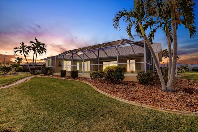 back house at dusk with a lanai and a yard