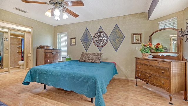 bedroom featuring ceiling fan, multiple windows, light hardwood / wood-style flooring, and connected bathroom