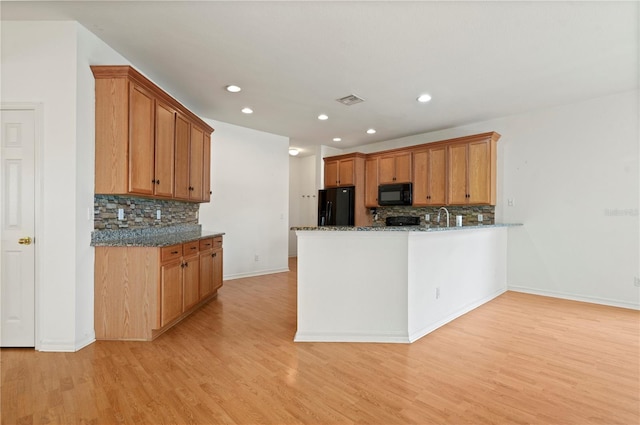 kitchen featuring backsplash, light hardwood / wood-style floors, dark stone counters, and black appliances