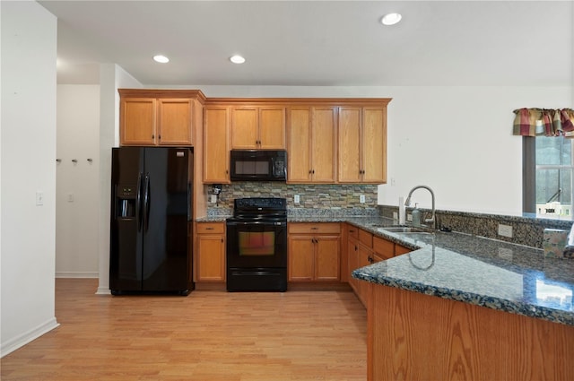 kitchen featuring black appliances, sink, light hardwood / wood-style flooring, dark stone countertops, and kitchen peninsula