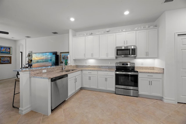 kitchen featuring kitchen peninsula, a breakfast bar, white cabinetry, appliances with stainless steel finishes, and light stone counters