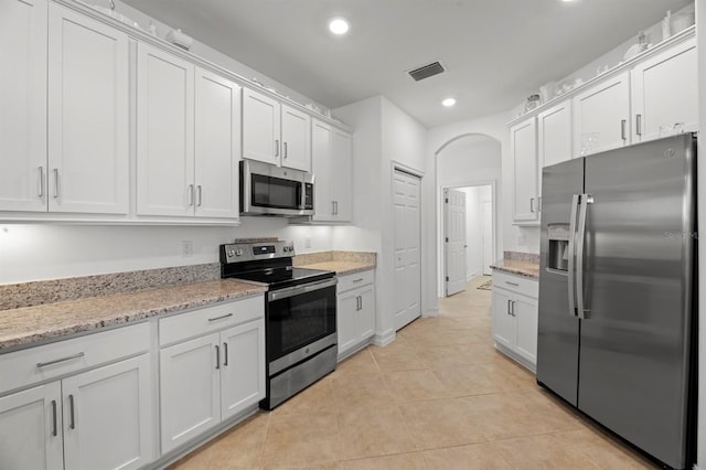 kitchen with stainless steel appliances, light stone countertops, light tile patterned floors, and white cabinets