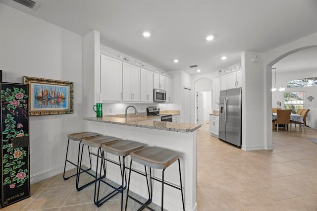 kitchen featuring appliances with stainless steel finishes, kitchen peninsula, white cabinetry, and light stone countertops