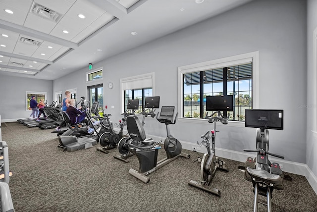 exercise room featuring coffered ceiling, carpet, and a high ceiling