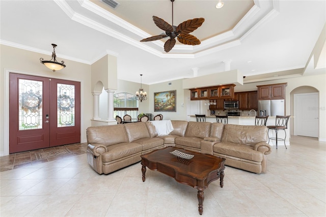 living room featuring french doors, ceiling fan with notable chandelier, crown molding, and a raised ceiling