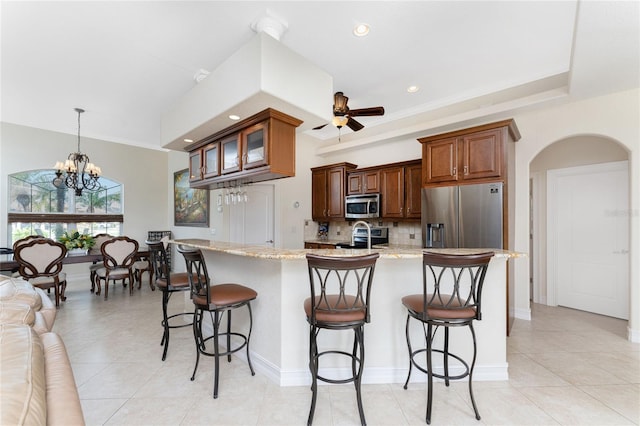 kitchen with a kitchen bar, decorative backsplash, hanging light fixtures, light stone countertops, and appliances with stainless steel finishes