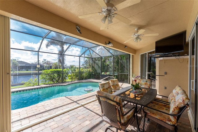 view of pool with a lanai, ceiling fan, a patio, and a water view