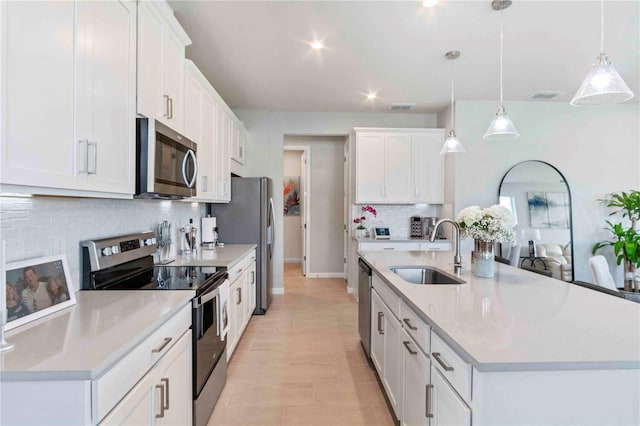 kitchen with appliances with stainless steel finishes, pendant lighting, an island with sink, sink, and white cabinets