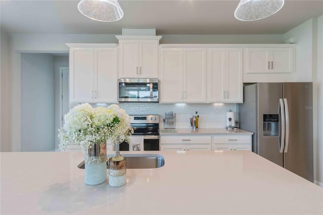 kitchen featuring stainless steel appliances, white cabinetry, hanging light fixtures, and decorative backsplash